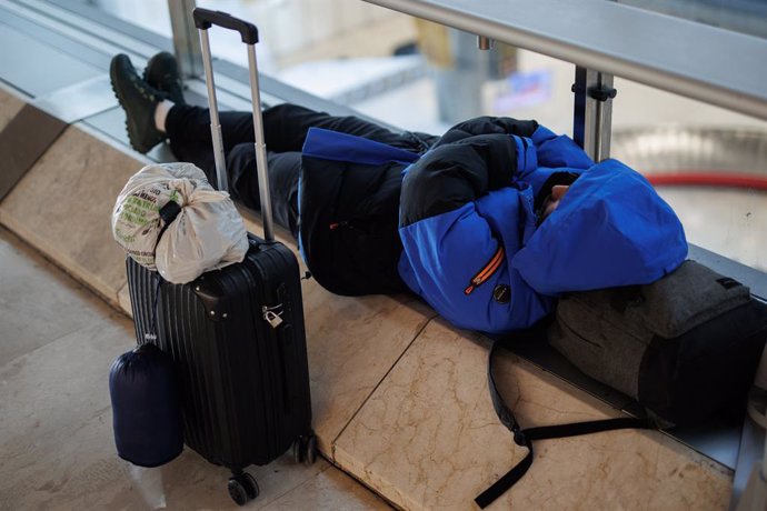 Archivo - Una persona espera tumbada junto a su maleta en la T4 del aeropuerto Adolfo Suárez Madrid-Barajas.