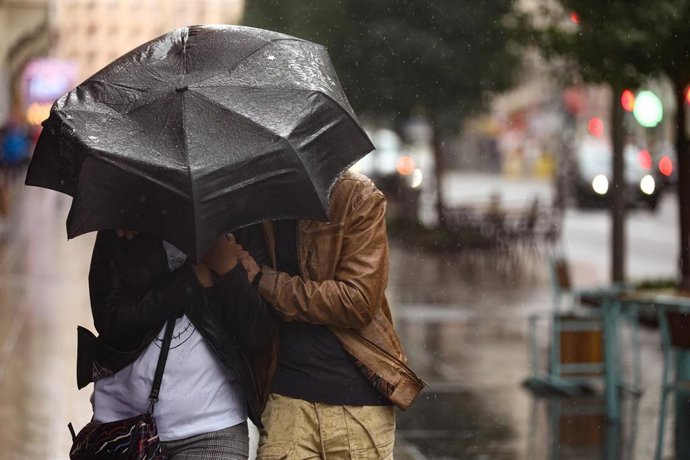 Archivo - Una pareja se protege de la lluvia con un paraguas, en la calle Gran Vía, a 20 de octubre, en Madrid (España). 