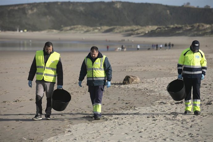 Archivo - Varios hombres recogen pellets en la playa de Salinas, a 13 de enero de 2024, en Castrillón, Asturias.