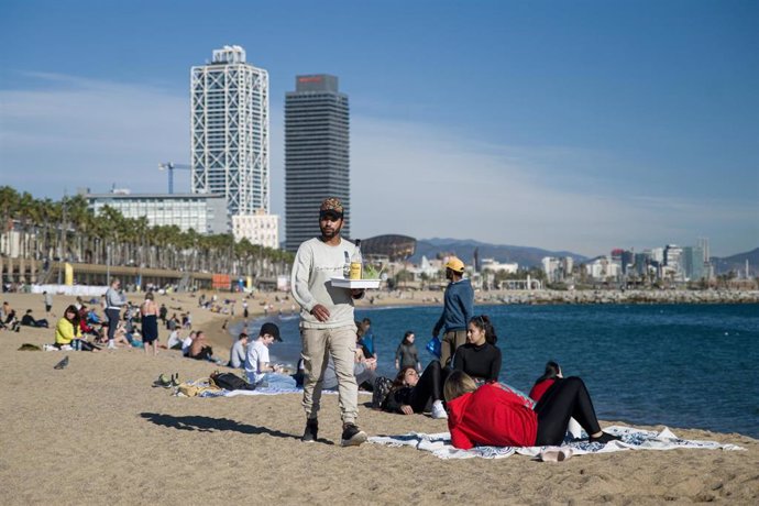 Archivo - Un camarero lleva bebidas a las personas que disfrutan en la playa de la Barceloneta