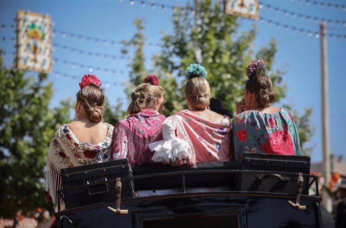 Archivo - Cuatro mujeres vestidas de flamenca con mantones en un carruaje a caballo, en el Real de la Feria, en una foto de archivo.