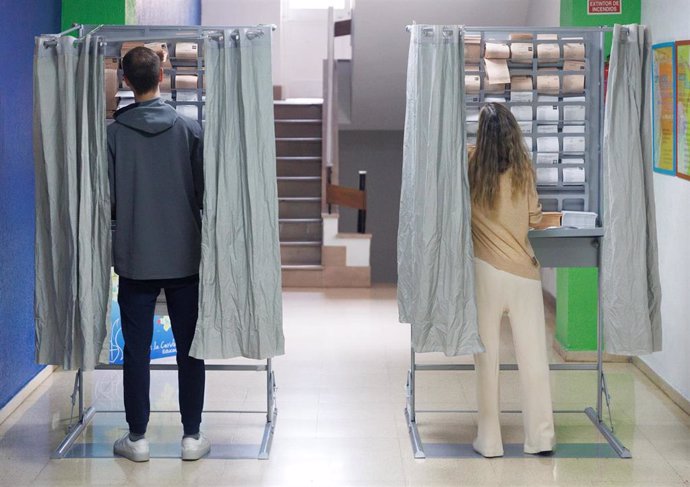 Archivo - Dos personas ejercen su derecho a voto en una cabina en un colegio electoral