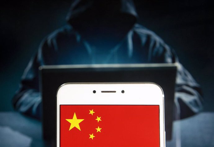 Archivo - Imagen de un pirata informático junto a la bandera de China en un teléfono móvil