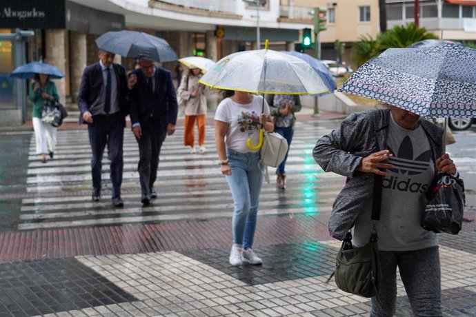 Archivo - Viandantes con paraguas cruzando un paso de peatones.