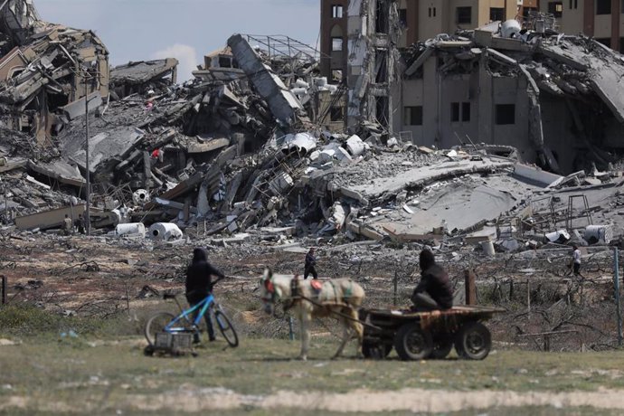 Un grupo de palestinos entre edificios destruidos por los bombardeos del Ejército de Israel cerca del campamento de refugiados de Nuseirat, en el centro de la Franja de Gaza