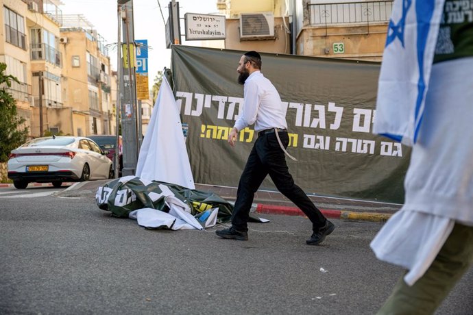 Archivo - March 16, 2023, Bnei Brak, Israel: An orthodox man passes next to a protest against the reform banner that says 'Haredim/anxious for the fate of the country, Torah as well as martial theory/Torah' during the demonstration. The soldiers opened a 