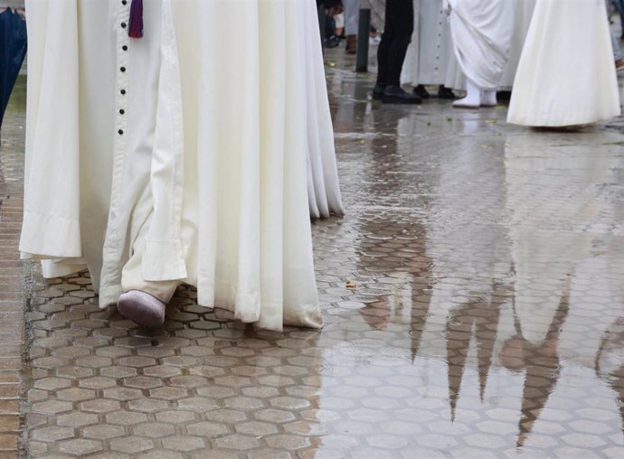 Un nazareno caminando sobre la acera mojada por la lluvia durante la Semana Santa.
