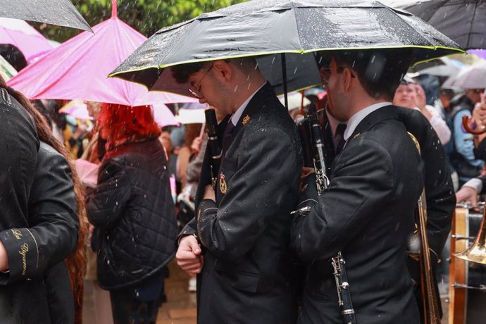 Imagen de músicos guarecidos bajo paraguas durante la Semana Santa de Sevilla 2024.