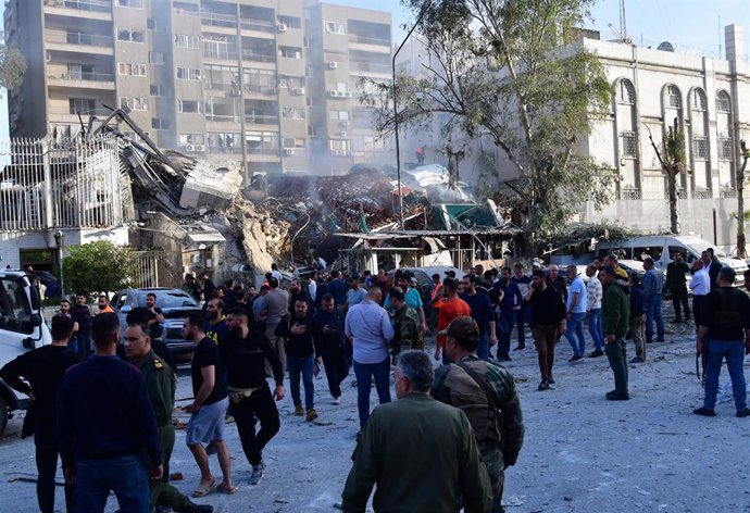 Un grupo de personas congregada alrededor de los desperfectos del Consulado iraní en Damasco tras un ataque aéreo atribuido a Israel.