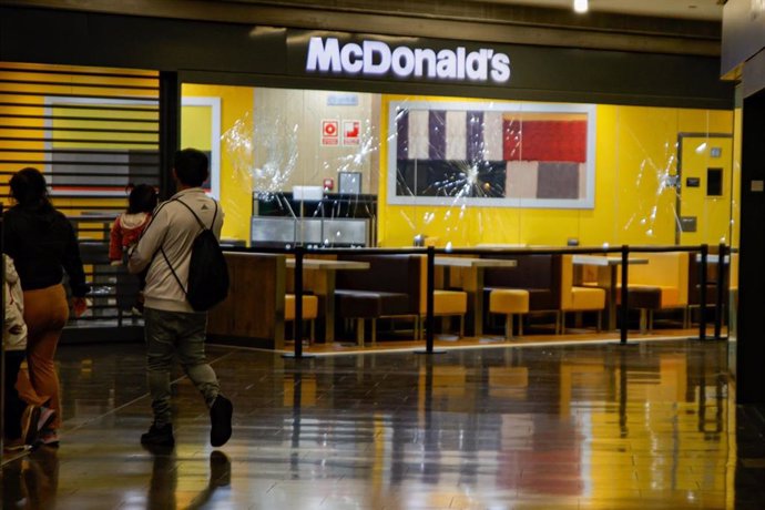 Dos personas pasan delante del escaparate del McDonald's con los cristales rotos en el centro comercial Màgic Badalona, a 27 de marzo de 2024, en Badalona, Catalunya (España). Un hombre ha sido detenido este miércoles en el centro comercial Màgic Badalona