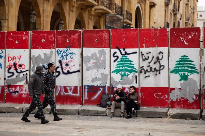 Archivo - January 27, 2020, Beirut, Beirut, Lebanon: Beirut, Lebanon. Lebanese police walk past two people sitting on a graffitied security wall around the government buildings in Downtown Beirut, as the government votes on the 2020 budget. Anti governmen