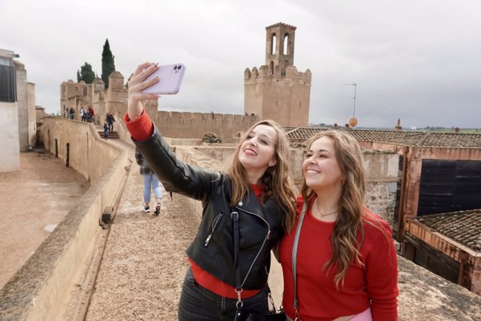 Dos turistas se hacen una foto en la Alcazaba con la Torre de Espantaperros de fondo.