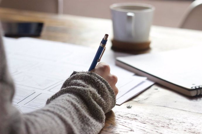 Una estudiante escribe con un bolífrago encima de una mesa