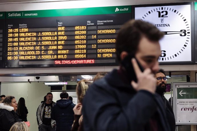 Archivo - Vista de una pantalla informativa con muchos viajes 'demorados', y una persona hablando por teléfono móvil, en la estación de Madrid-Chamartín-Clara Campoamor