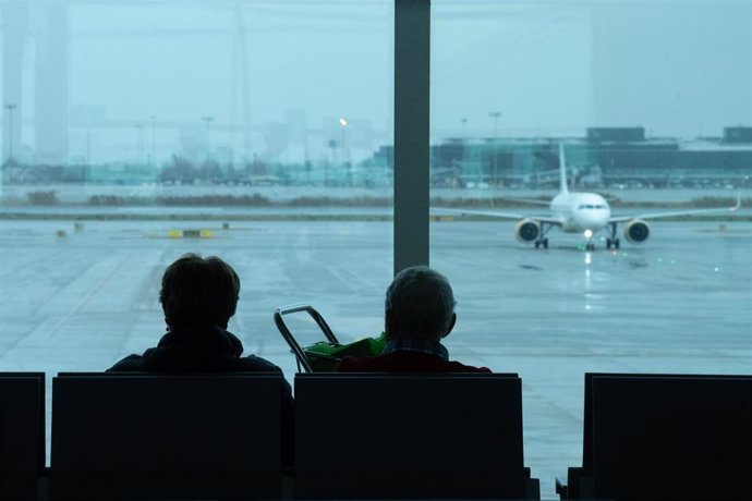 Archivo - Dos personas esperan sentadas frente a un avión aparcado en la pista del aeropuerto de El Prat.