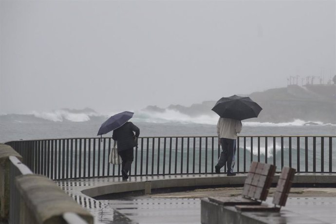 Archivo - Dos personas caminan con un paraguas al lado de la playa del Orzán,A Coruña.