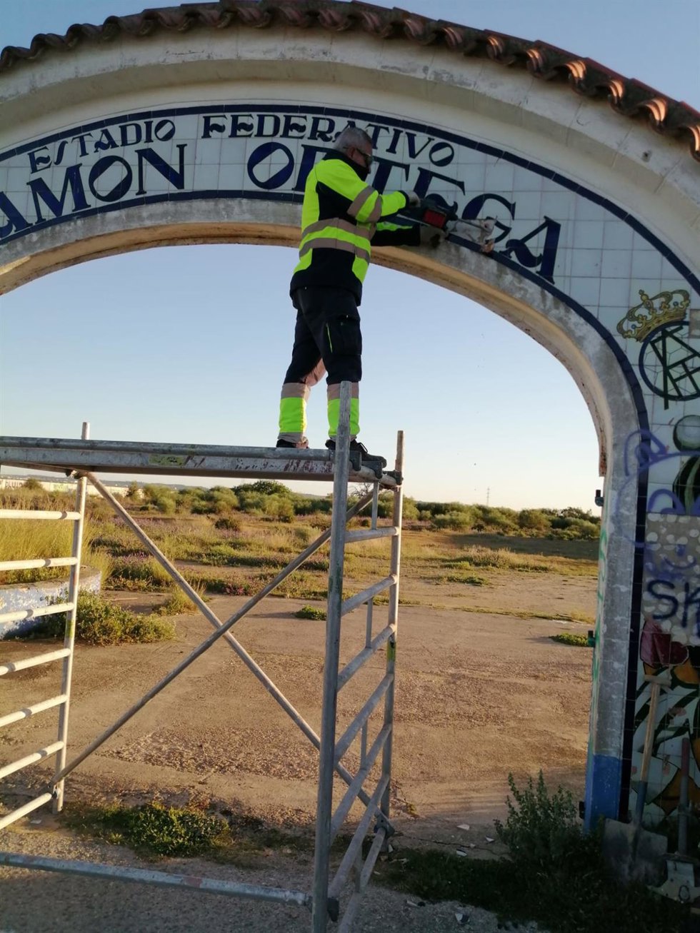 Operario municipal eliminando el nombre de Ramón Ortega, relacionado con el franquismo, del estadio deportivo de Puerto Real