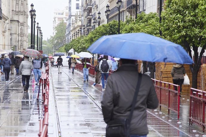 Archivo - Varias personas por con sus parágüas en parte del trayecto de la Carrera Oficial durante la vuelta de la lluvia a Sevilla en plenos montaje de los palcos para la Semana Santa, archivo