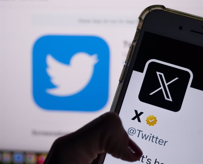Archivo - La app X en la pantalla de un móvil con el logo de la antigua Twitter de fondo 