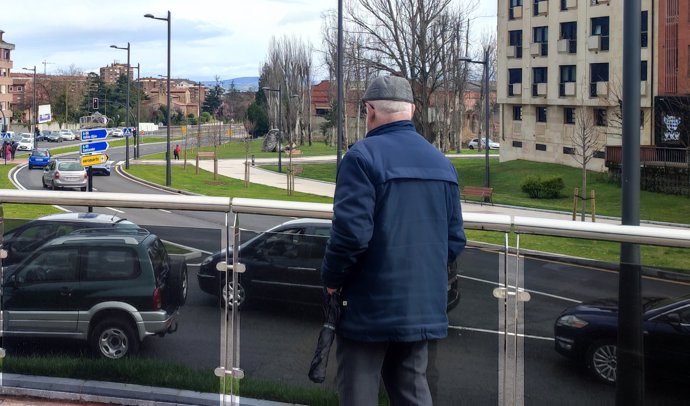 Una persona mayor observa el tráfico en la glorieta de la Cruz Roja de Oviedo, con la iglesia de San Julián de los Prados al fondo. Jubilado, pensión, pensionista.