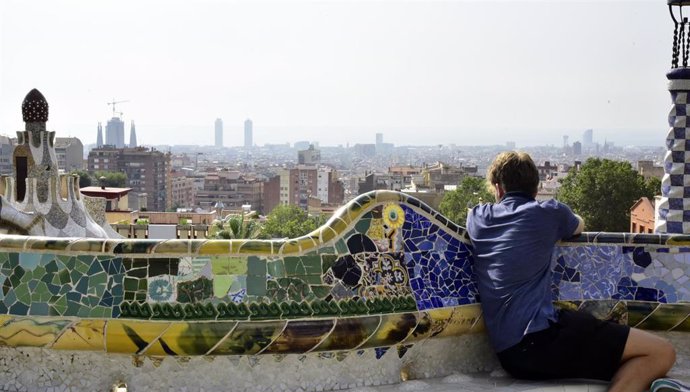 Archivo - Una persona sentado en uno de los asientos decorados con mosaicos de Gaudí ubicados en el Park Güell. Archivo.
