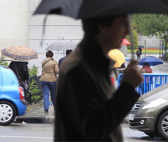 Archivo - Ciudadanos se protegen de la lluvia bajo un paraguas. Imagen de archivo