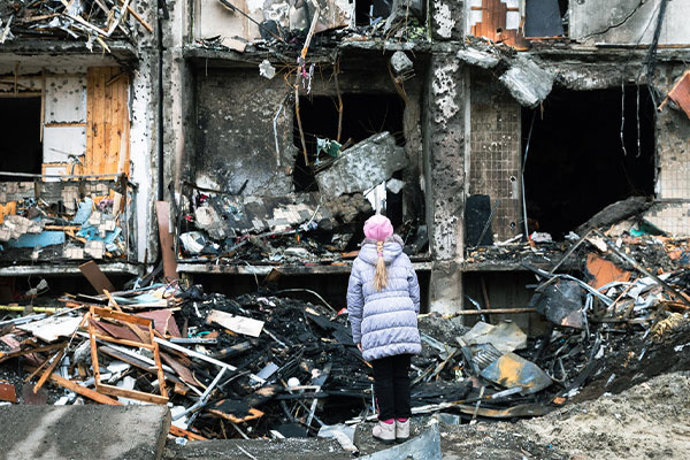 Archivo - Una niña observa un edificio destrozado