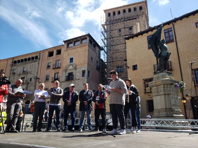 Momento de la lectura del Estatuto de la Comunidad Autónoma, por parte de un grupo de adolescentes, junto al delegado de la Junta en Segovia, José Luis Sanz Merino y otras autoridades. Detrás, la estatua de Juan Bravo.