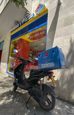 Archivo - Una moto de Domino's Pizza aparcada al lado de un establecimiento de la franquicia en Madrid