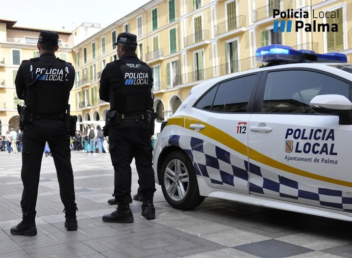 Dos agentes de la Policía Local de Palma de espaldas junto a un coche oficial.