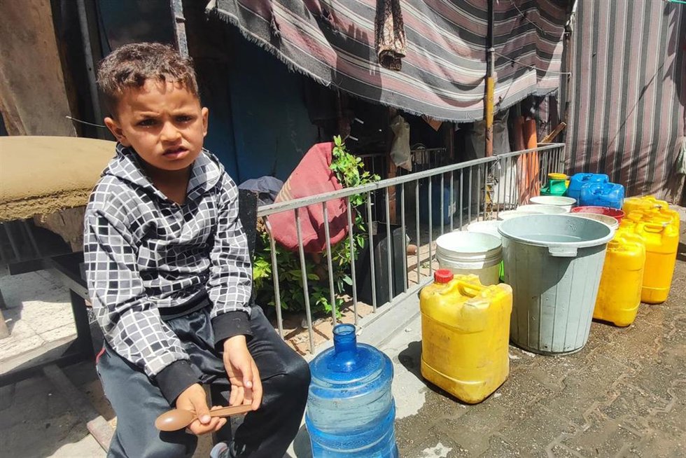 Un niño palestino junto a garrafas para agua en Gaza