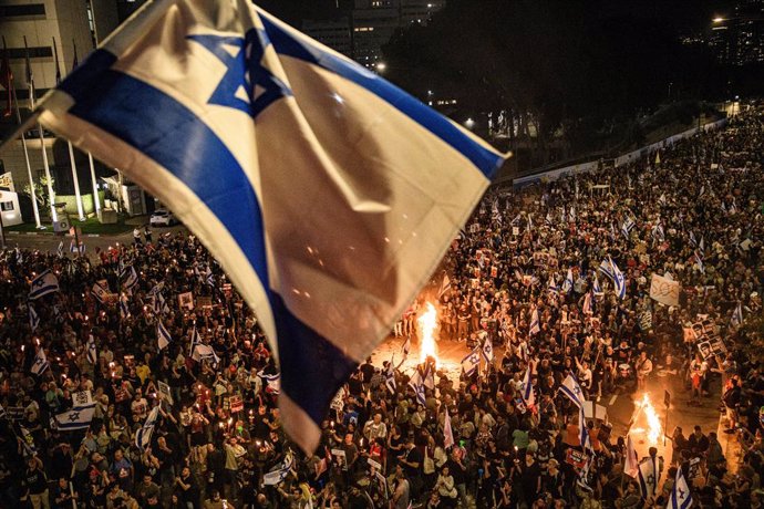 March 30, 2024, Tel Aviv, Israel: Tens of thousands gather around bonfires below a waving Israel flag during the demonstration. Tens of thousands of people demonstrated with the hostages families against Prime Minister Benjamin Netanyahu in Tel Aviv, dema