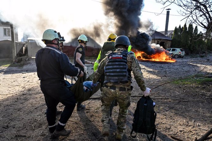 05 April 2024, Ukraine, Zaporizhzhia: Rescue workers and police carry an injured man on a stretcher while a column of smoke rises in the background. Photo: -/Ukrinform/dpa