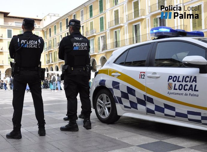 Dos agentes de la Policía Local de Palma de espaldas junto a un coche oficial.
