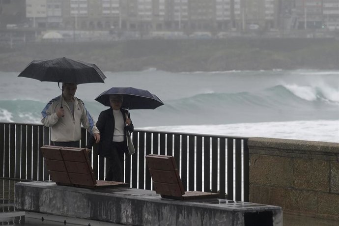 Archivo - Dos personas caminan con un paraguas al lado de la playa del Orzán, a 22 de enero de 2024, A Coruña, Galicia (España). La dirección xeral de Emerxencias de la Xunta ha activado hoy la alerta naranja por temporal costero en todo el litoral gall