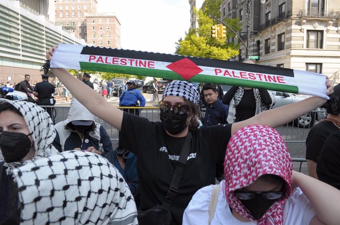 30 April 2024, US, New York: A pro-Palestine protester holds up a scarf that says, "Palestine," at a rally outside of an entrance at Columbia University. Overnight, students and protesters inside the campus occupied a university building named Hamilton Ha