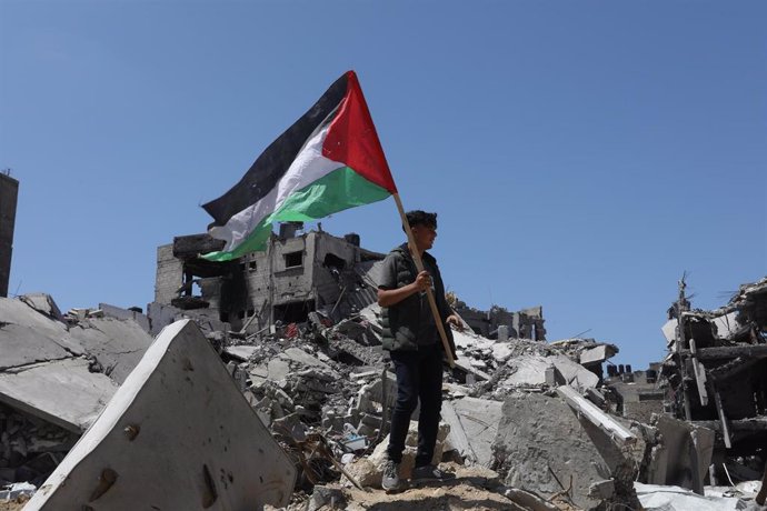 Un joven sujeta una bandera palestina sobre los restos de edificios bombardeados por Isarel en la Franja de Gaza