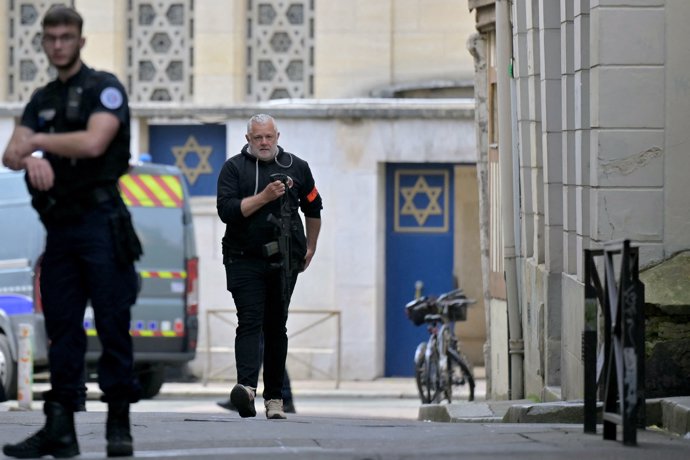 17 May 2024, France, Rouen: A policeman holds a rifle as he walks past the entrance of a synagogue where French police killed an armed man who had tried to set the fire on the building. Photo: Lou Benoist/AFP/dpa