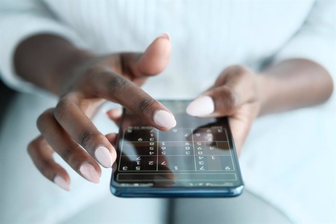 Archivo - Mujer jugando al sudoku con un móvil.