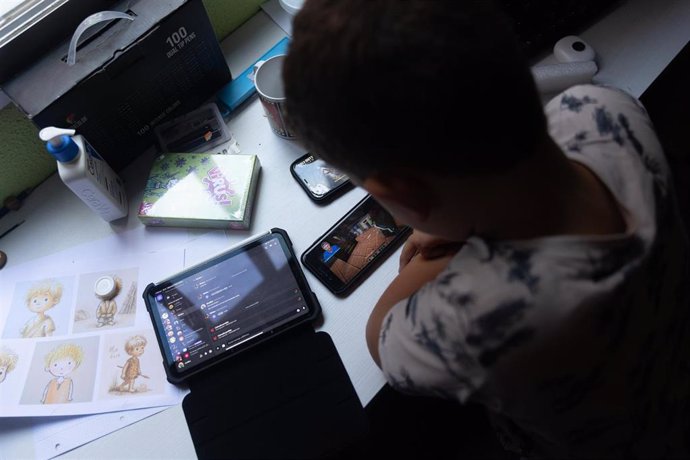 Archivo - Un niño usa el teléfono móvil y una tablet