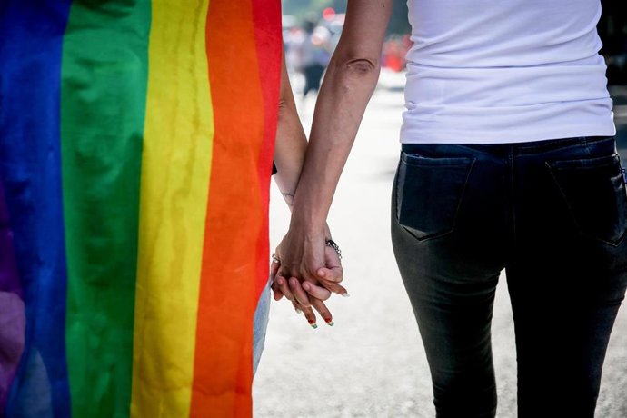 Archivo - Una pareja cogida de la mano con la bandera LGTBI