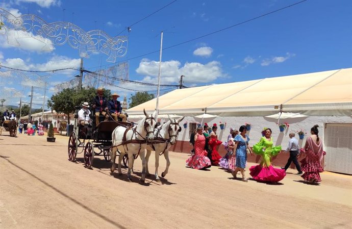 Un grupo de mujeres y un coche de caballos pasan junto a una caseta en la Feria de Córdoba.