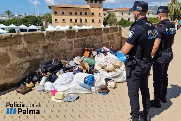 Dos miembros de la Policía Local de Palma, ante varios objetos abandonados por los vendedores de venta ambulante ilegal.