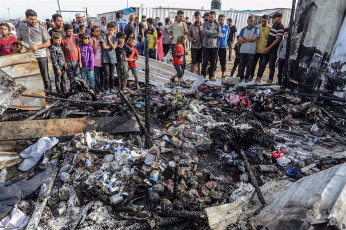 Un grupo de palestinos junto a tiendas quemadas en un campo de desplazados de Rafá, en la Franja de Gaza