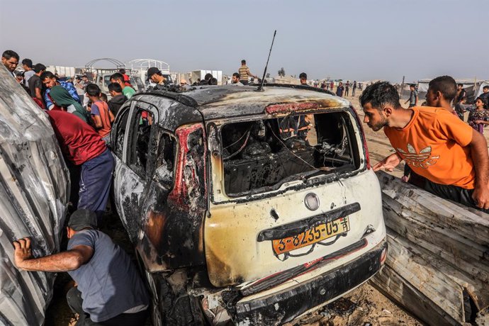 27 May 2024, Palestinian Territories, Rafah: Palestinians inspect a burnt car after an Israeli air strike, which resulted in numerous deaths and  injuries, in the Al-Mawasi area, which was bombed with a number of missiles on the tents of displaced people 