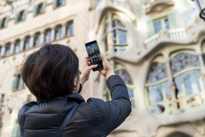 Archivo - Una turista realiza una fotografía con su teléfono móvil a la Casa Batlló de Barcelona.