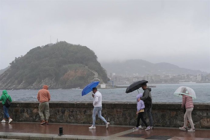 Archivo - Varias personas caminan con paraguas en la playa de Ondarreta, en San Sebastián