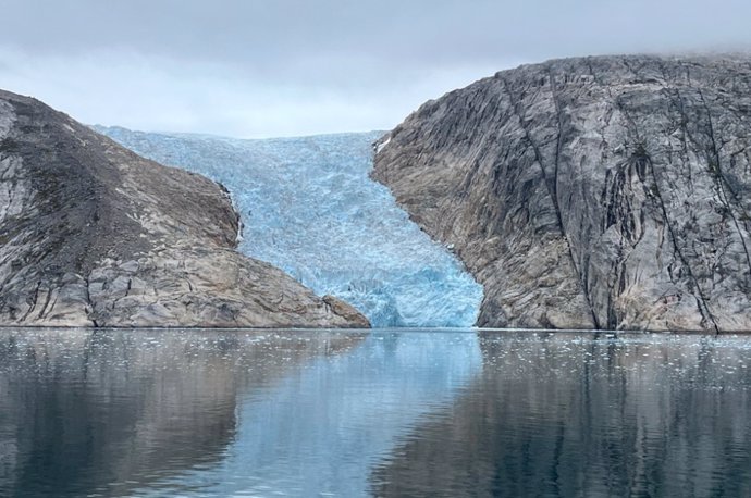 Entre dos colinas rocosas, un glaciar azul helado fluye hacia abajo y se encuentra con el agua.