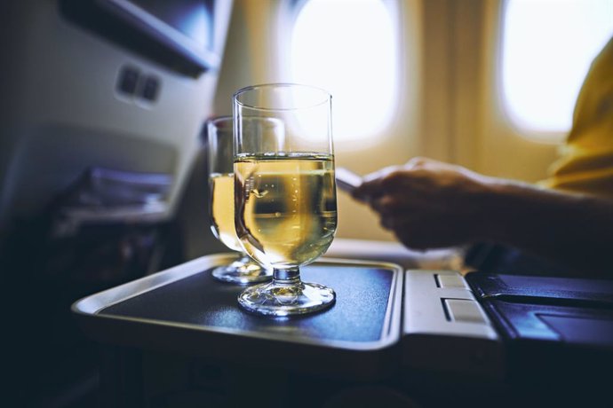 Archivo - Dring during flight. Two drinking glasses of sparkling wine against airplane window.