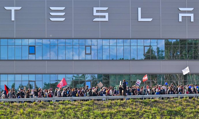 11 May 2024, Brandenburg, Gruenheide: Environmental activists walk past the Tesla plant during a protest against Tesla. After sometimes violent clashes on May 10, 2024 at the Tesla factory site in Gruenheide near Berlin. 